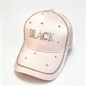 Gros plan sur une casquette en satin rose avec lettrage BLACK et strass brillants.