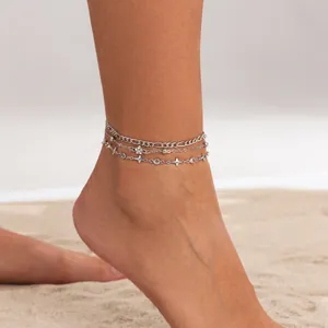 Detailed view of multilayer silver anklets with chain and star details on soft beach sand