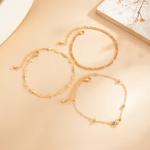 Close-up of three gold-tone minimalist chain anklets with star and flower charms