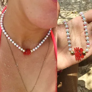 Détail d'un collier de perles orné d'un pendentif homard en verre rouge vif artisanal.