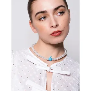Gros plan d'un collier de perles blanches avec un pendentif en verre bleu sur un modèle.