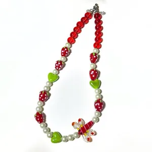 Détail d'un collier de perles fait main avec des breloques fraise et libellule colorées