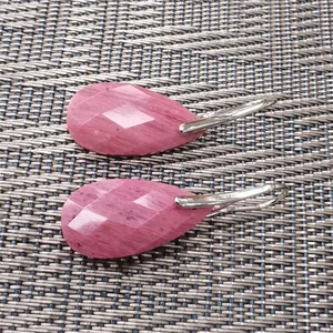 Macro detail of faceted pink pear-shaped teardrop stone earrings on textured background