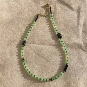 Detail view of natural stone beaded necklace with green, blue, and black beads on fabric