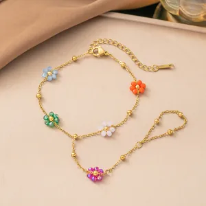 Dettaglio bracciale da mano in acciaio dorato con fiori di perline colorate e catena.