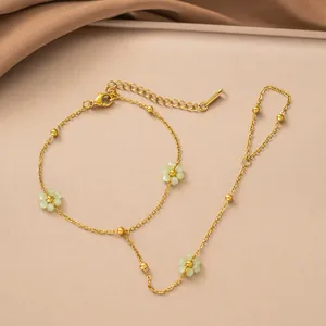Dettaglio di una catena da mano in acciaio dorato con ciondoli a forma di fiori verdi.