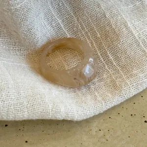 Minimalist amber-toned resin geometric oval ring showcased on textured cream fabric