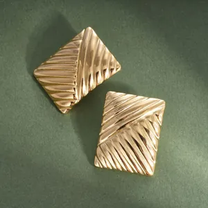 Close-up macro view of gold-plated rectangular earrings with a ribbed texture design