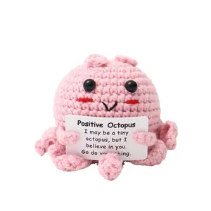 Handmade pink crochet positive octopus doll holding a motivational message card.