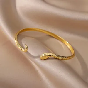 Detailopname van een vergulde slangenarmband met fijne schubtextuur op satijn.