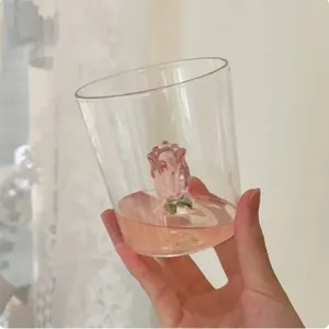 Detail of clear glass cup featuring a delicate 3D pink rose sculpture at the bottom