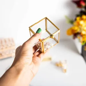 Close-up of a hand holding a mini square glass jewelry box with elegant gold frame