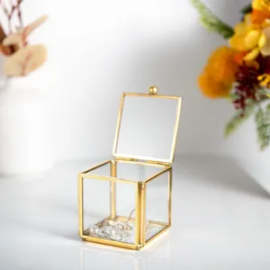 Close-up view of a small glass jewelry box with a gold metal frame and an open lid
