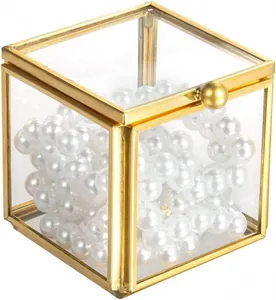 Close-up of a square gold metal and glass jewelry box filled with white pearls