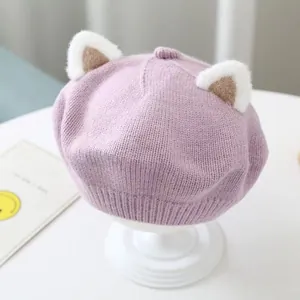Close-up of children's knitted beret featuring plush cat ear details and soft pink knit.