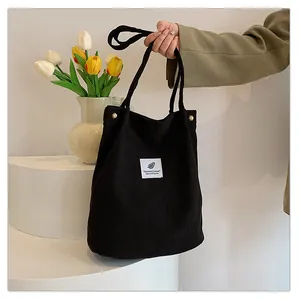 Mano che tiene una borsa tote in velluto a coste nera minimalista in un ambiente elegante