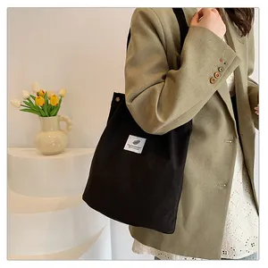 Vista laterale di una borsa tote in velluto a coste nera indossata con un blazer beige