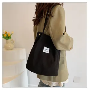 Vista laterale di una modella che porta una borsa tote in velluto a coste nera con etichetta.