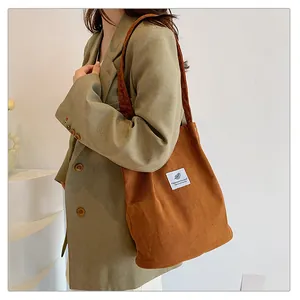 Dettaglio ravvicinato della borsa tote in velluto a coste marrone con modella in blazer verde.