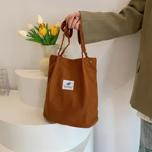 Dettaglio della borsa tote in velluto a coste marrone tenuta in mano, trama e etichetta