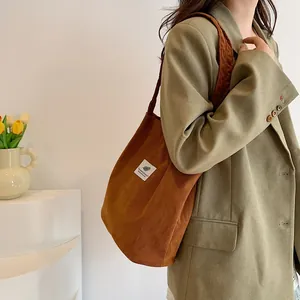 Dettaglio di una borsa a tracolla in velluto a coste marrone indossata da una modella.