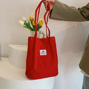 Vista dettagliata di una borsa tote in velluto a coste rosso vivace tenuta in un ambiente elegante.
