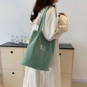 Primo piano di una modella con una borsa tote in velluto a coste verde salvia in un interno