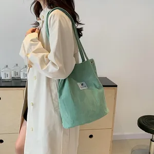 Dettaglio di una borsa a tracolla in velluto a coste verde indossata da una persona.