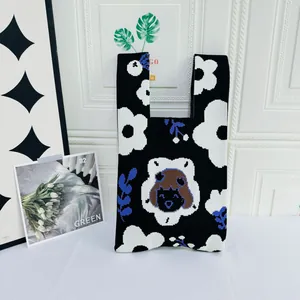 Detailed view of black knit tote bag with large white floral patterns and central character.