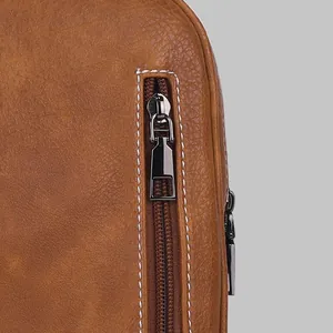 Macro view of high-quality brown leather texture and sturdy metal zipper on chest bag.