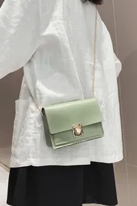 Close-up of mint green chain crossbody bag with push-lock on white linen shirt.