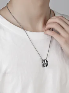 Detailopname van een herenketting van titaniumstaal met dubbele ringhanger op wit shirt.