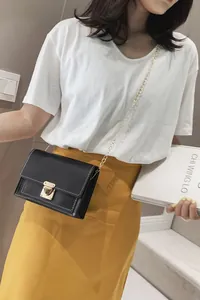 Elegant black small square crossbody bag with gold chain strap and lock closure on model