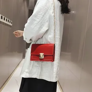 Detail view of a vibrant red square crossbody bag with a gold metal lock and chain strap
