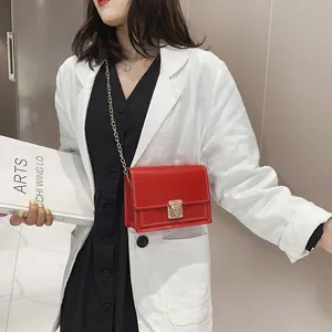 Detail of a vibrant red small square crossbody bag with gold chain strap on a white blazer model