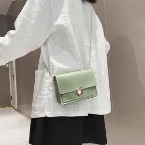 Detailed view of light green small square bag with chain strap worn crossbody.