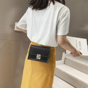 Stylish woman wearing a black square crossbody bag with a gold chain in a modern setting.