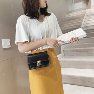 Fashionable small black square crossbody bag with gold chain strap worn by a model