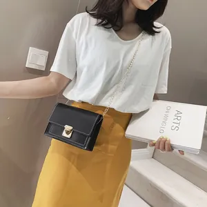 Modern black square crossbody bag with gold chain strap and latch closure worn by a model