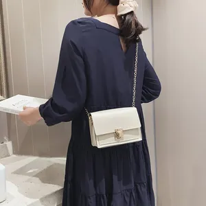 Elegant cream-white crossbody chain bag with gold lock shown on model in navy blue dress