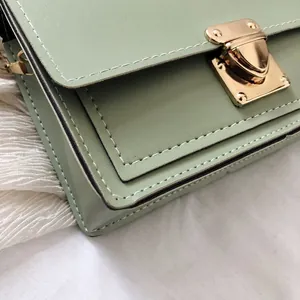 Close-up of light green crossbody bag with gold latch and white stitching details
