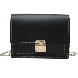 Close-up detail of a minimalist black faux leather crossbody bag with gold lock and chain