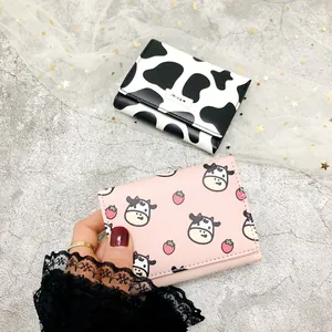 Close-up of cute tri-fold mini wallets with cow print and strawberry patterns for women.