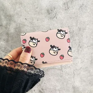 Close-up of pink mini trifold wallet with cute cartoon cow and strawberry pattern