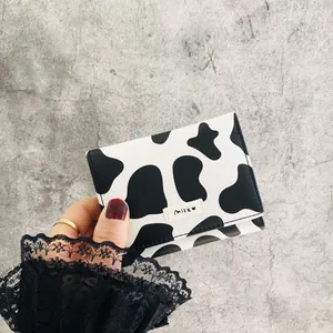 Close-up of a mini cow print tri-fold wallet held in hand against grey background