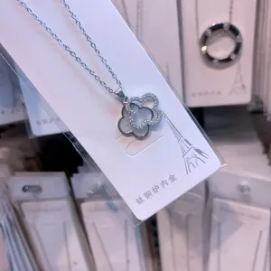 Macro detail of a titanium steel four-leaf clover necklace with white shell and crystal inlay