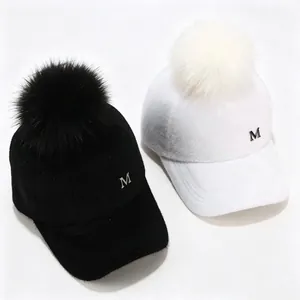 Vista detallada de gorras de béisbol de felpa en blanco y negro con pompones y el logo M