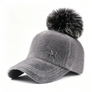 Vista detallada de gorra de béisbol de felpa gris con pompón de piel y logo M