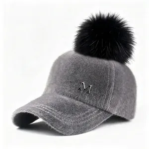 Detalle de gorra de béisbol gris de peluche con pompón negro y logotipo metálico M