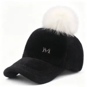 Detalle de gorra de béisbol negra peluda con pompón blanco y logotipo M plateado frontal
